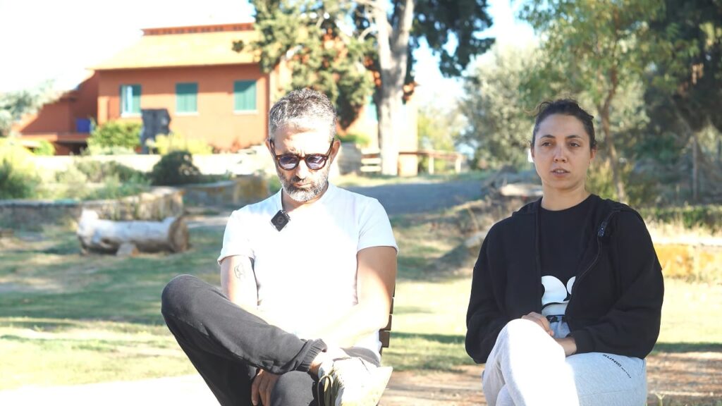 Lara e Antonio, che si guardano con espressione seria ma speranzosa, seduti in un ambiente naturale, a simboleggiare il loro percorso insieme.